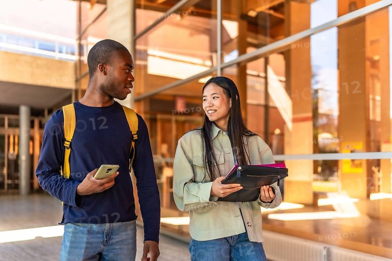 Multiracial chinese and african american students walking along the university talking distracted
