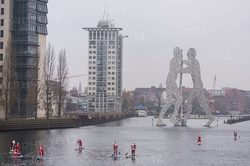 Water sports enthusiasts dressed as Santas ride SUPs on the Spree in front of the Molecule Man in Berlin on 14 December 2024