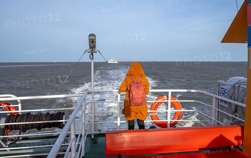Norderney, Lower Saxony, Germany - The ferry Frisia IV operated by AG Reederei Norden-Frisia sails from Norderney to Norddeich. Norderney is one of the East Frisian Islands in the North Sea. In front, a woman in a winter coat stands at the railing and looks out to sea