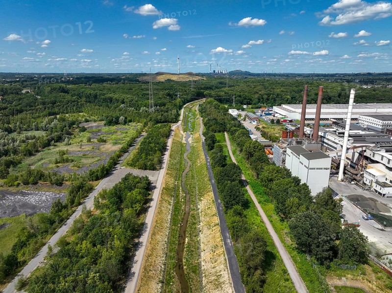 Bottrop, North Rhine-Westphalia, Germany, Renaturalised Boye, the tributary of the Emscher, was transformed into a near-natural watercourse, flood protection through newly designed floodplains, the Boye is now free of wastewater after the construction of a parallel sewer, is part of the Emscher river system and thus part of the Emscher conversion, was previously an open, above-ground wastewater channel, mixed water channel with surface water and wastewater. Wind turbine on Mottbruch spoil tip at the back. On the right, industrial area with chimneys on Essen territory, Europe