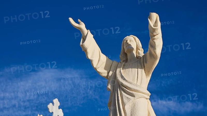 A stone statue of Jesus with outstretched arms against a blue sky, Agios Nikolaos church, cemetery, Pigadia, town and harbour, Pigadia Bay, main town, Karpathos, Dodecanese, Greek Islands, Greece, Europe