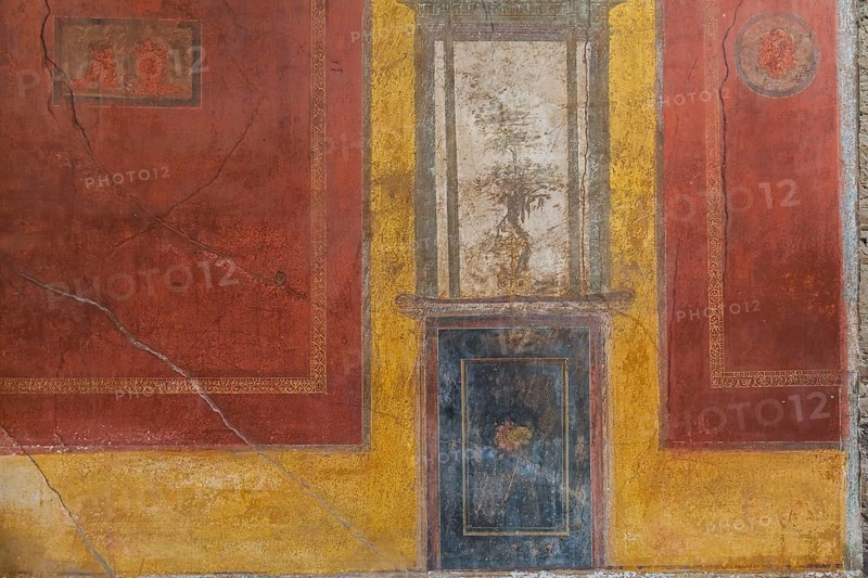 Close-up of reddish brown, blue and white frescoes on yellow wall of old residential building at the ancient ruins of Pompeii, Campania region, Italy, Europe