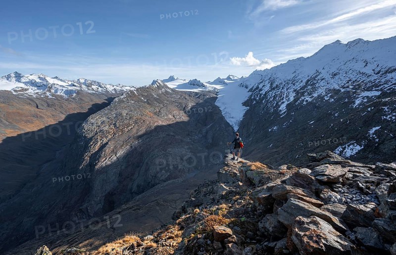 Mountaineer standing on a rock, surrounded by an impressive mountain landscape with snow-covered peaks in autumn View of Gurgler Ferner with summit Hochwilde and Falschungsspitze, Ötztal Alps, Tyrol, Austria, Europe