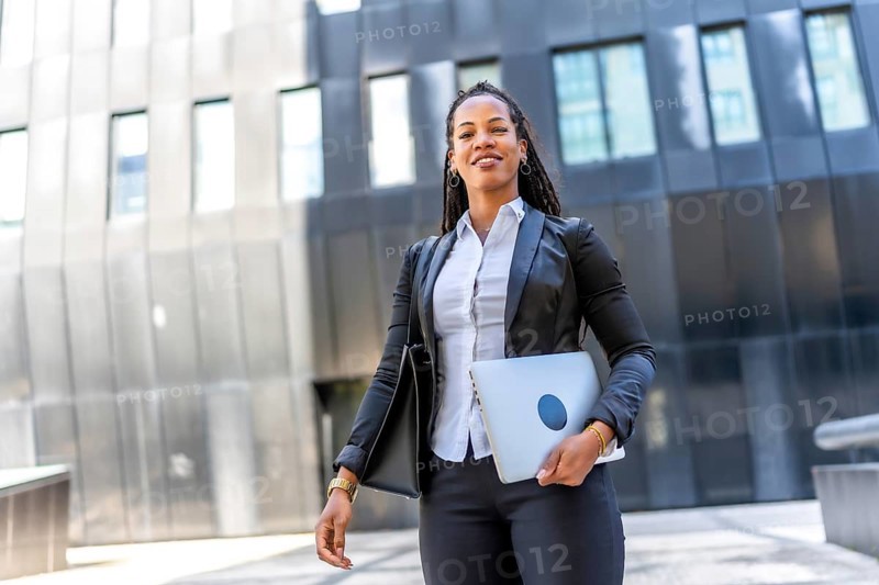 Professional young latin businesswoman standing carrying laptop in the city next to a modern financial building