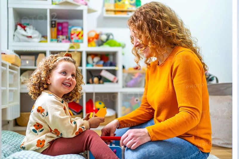 Caucasian adult mother and girl playing with toys sitting in the bedroom at home