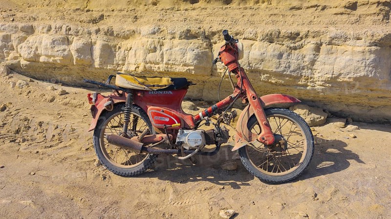 An old Honda C50 motorbike stands abandoned in front of a rocky cliff, Paralia Agios Theodoros beach, Arkasa, Karpathos, Greece, Europe