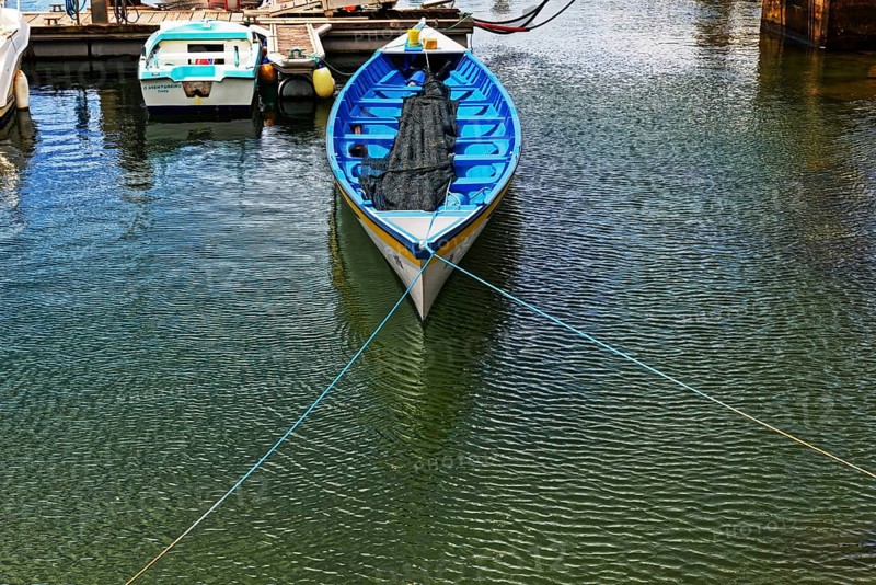 A blue fishing boat with a net lies quietly in a sunny harbour, small town of Vila Franca do Campo, Sao Miguel, Azores, Portugal, Europe
