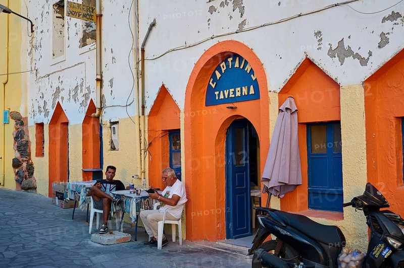 People sitting in front of a colourful facade of a taverna and enjoying their time on the street, Mandraki, Nisyros, Dodecanese, Greek Islands, Greece, Europe