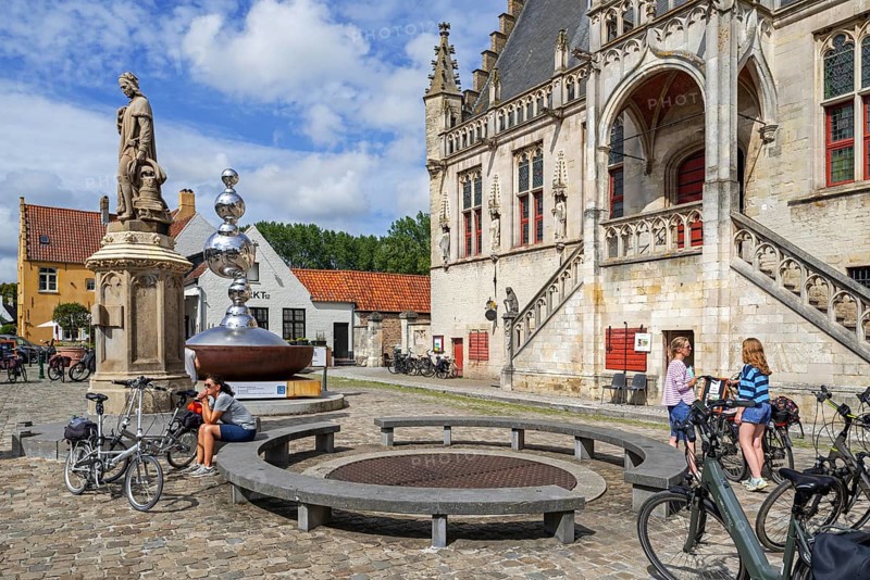 Statue of Jacob van Maerlant and cyclists in front of the Brabantine Gothic town hall in the city Damme in summer, West Flanders, Belgium, Europe