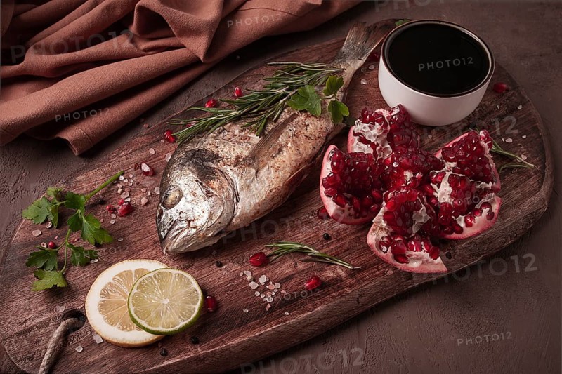 Fried dorado fish, with spices and herbs, on a wooden board, pomegranate sauce, close-up, no people