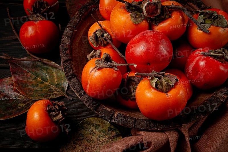 Fresh persimmon, in a wooden plate, top view, no people