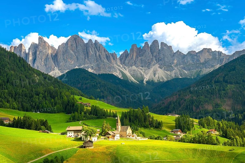 Green meadows, pine forests, and the iconic odle mountains rising majestically behind the church of santa maddalena in val di funes, italy