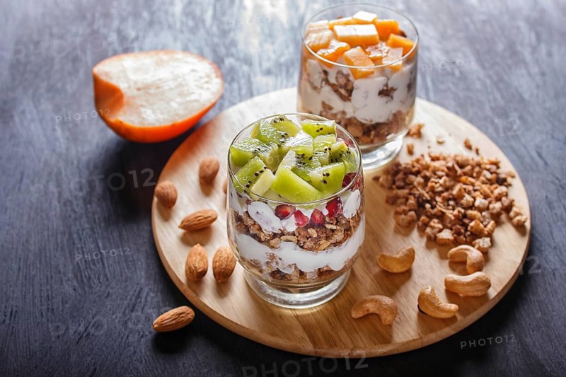 Dessert with greek yogurt, granola, almond, cashew, kiwi and persimmon on wooden background. close up