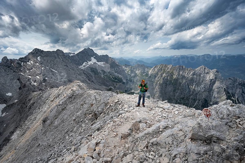 Mountaineer with helmet on a narrow rocky path, crossing the Jubiläumsgrat, view of Zugspitze and Höllental in steep rocky mountain landscape, ascent to Alpspitze via the south-west climb, Wetterstein range, Bavaria, Germany, Europe