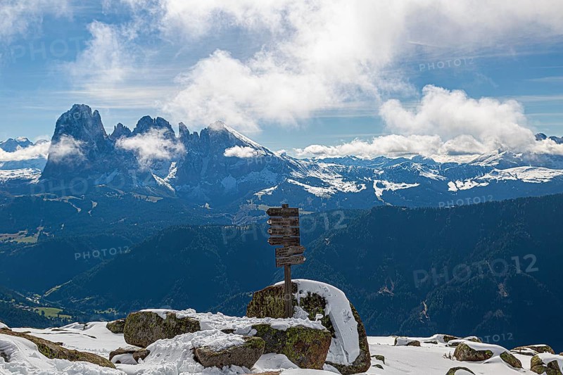 Snow-covered mountains under a blue sky with clouds and a wooden signpost with a view of the Lankofel mountain group in Val Gardena, South Tyrol, Italy, Europe