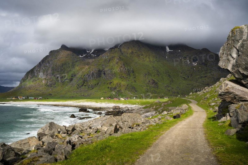Uttakleiv (Utakleiv) with mountains, in the foreground the hiking trail around the mountain Veggen. Beach, rocks and sea on the left. Cloudy sky with sun. Early summer. Uttakleiv, Vestvagoya, Lofoten, Norway, Europe