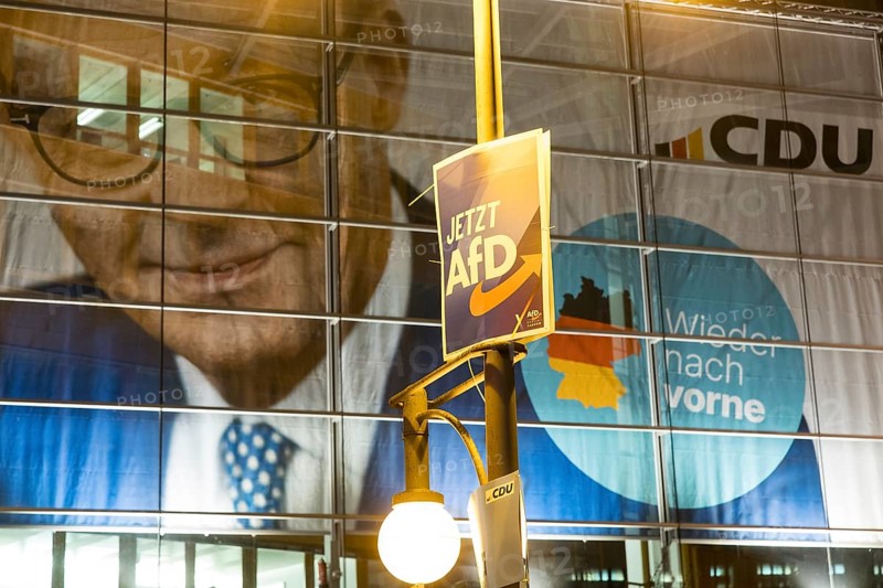 Banner with the likeness of Friedrich Merz behind an AfD election poster (now AfD) at the demonstration under the slogan Brandmauer statt Brandstifter / Asylrecht verteidigen in front of the Konrad-Adenauer-Haus, the party headquarters of the CDU, after a joint vote by the CDU and AfD in favour of a stricter migration policy introduced by party chairman Friedrich Merz. Berlin, 30.01.2025