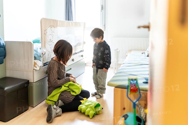 Mother and son playing together at home, preparing a dinosaur costume for a fun game in their bedroom