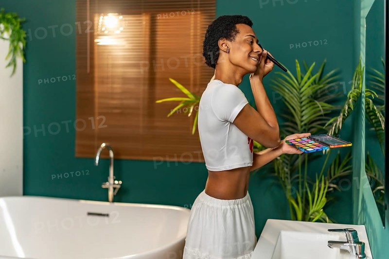 Gay latin man applying make up standing facing bathroom mirror at home