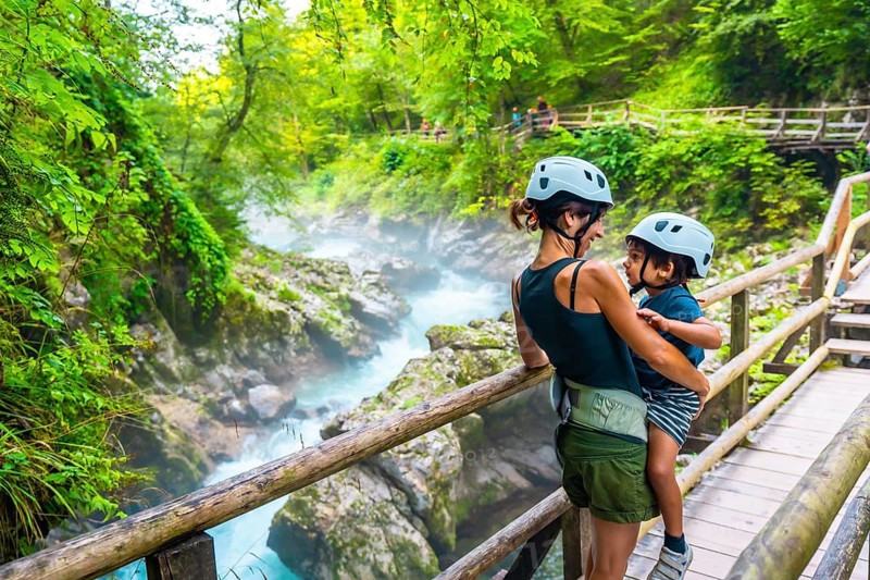 Mother holding her son while enjoying the breathtaking view of the turquoise radovna river flowing through the vintgar gorge near bled, slovenia