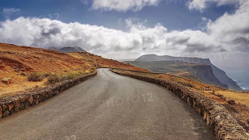 Serpentine road in a barren mountain landscape with clouds in the sky near the Mirador del Rio, Lanzarote, Canary Islands, Spain, Europe