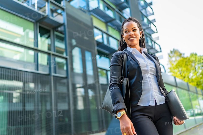 Confident cuban businesswoman walking out the block office carrying handbag and laptop