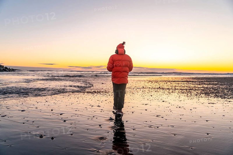 A man in an orange jacket walking at sunrise on Diamond Beach Iceland in winter