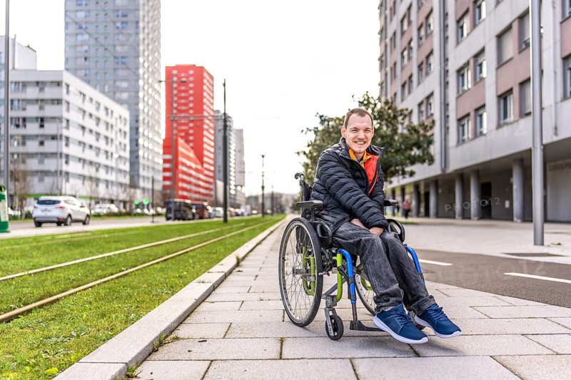 Portrait of a happy young man with disability in a wheelchair enjoying a sunny day in the city