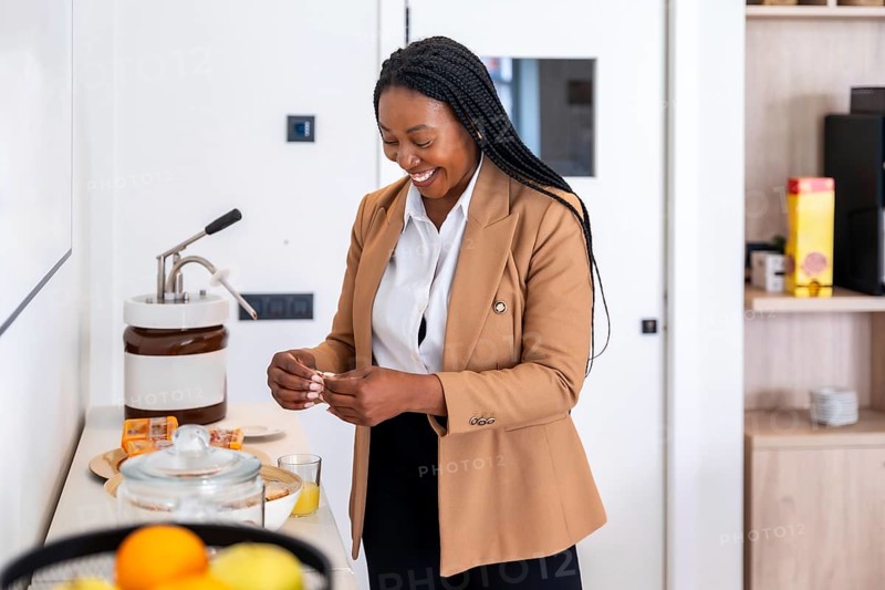 Smiling businesswoman preparing breakfast in hotel room during business trip, enjoying amenities and convenience