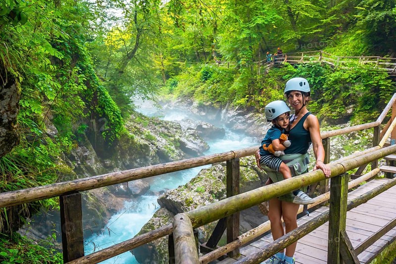 Mother carrying her child while visiting the stunning vintgar gorge near bled, slovenia, enjoying a breathtaking view of the turquoise river and lush forest