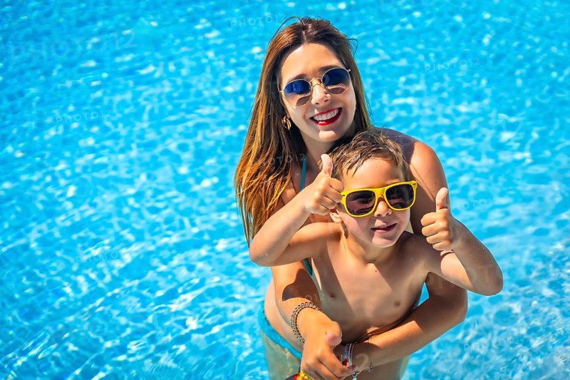 Happy mother and boy gesturing with thumbs up inside a blue pool water
