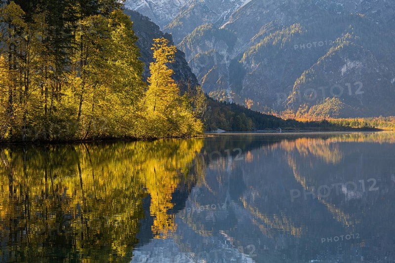 Lake Almsee in autumn with mountains reflected in the lake. Blue sky