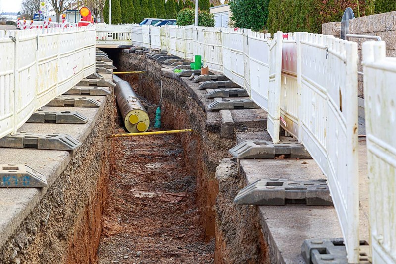 Construction site scene with district heating pipeline in a deep trench and white barriers