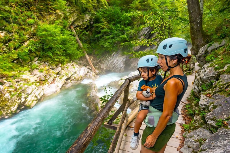 Mother carrying her son while observing stunning turquoise radovna river rapids flowing through vintgar gorge near bled, slovenia