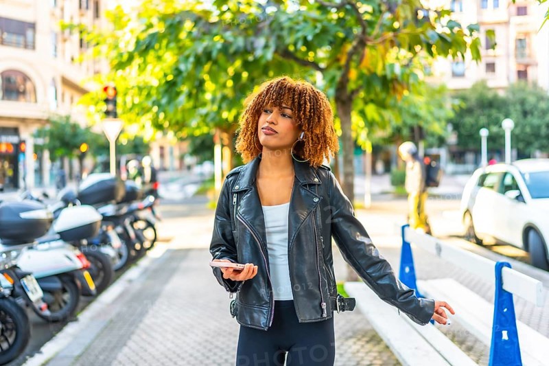Latin woman enjoy the city walking and listening to music using phone