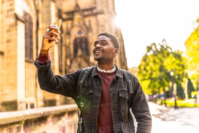 Happy african man walking along the city taking photos under the sunset