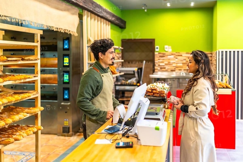 Elegant latin woman talking to salesman in a modern and artisan bakery