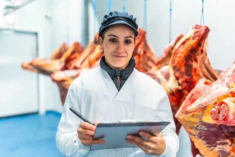 Portrait of a woman working in a meat processing factory writing notes in a clipboard