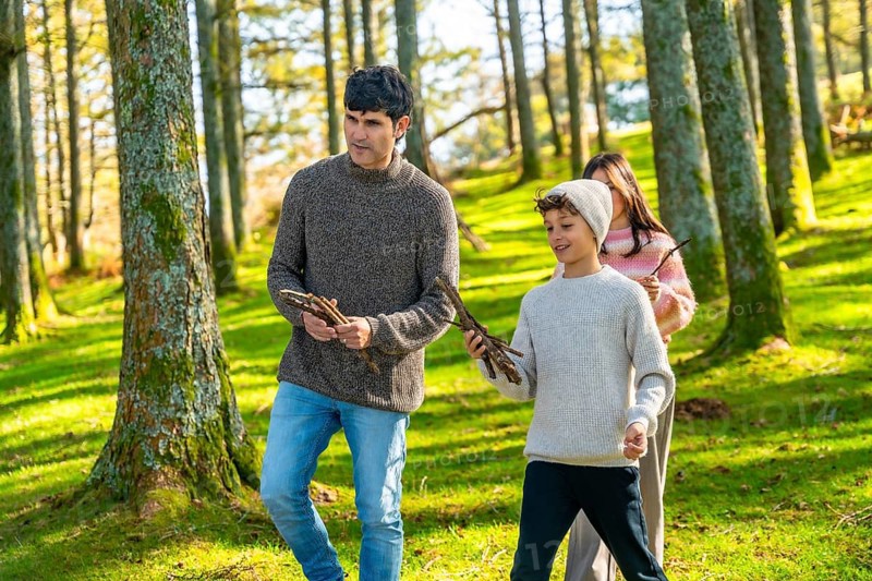 Caucasian father and two children collecting wood for camp fire while trekking in the forest