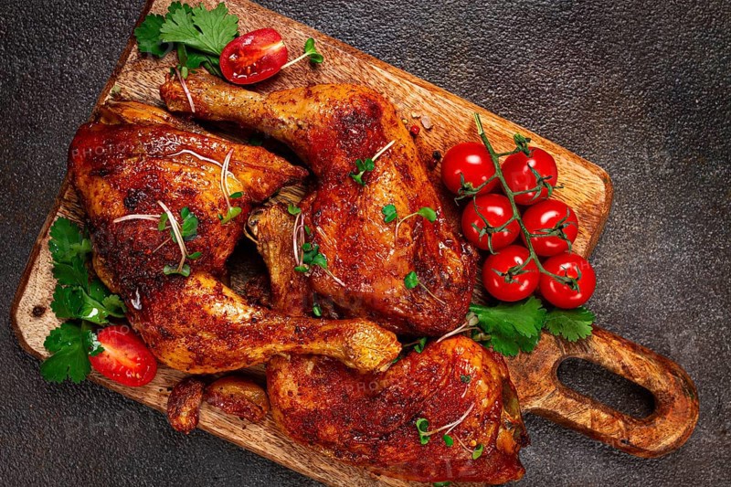 Grilled fried chicken legs, served with fresh cherry tomatoes, and herbs, on a wooden chopping board, homemade, no people