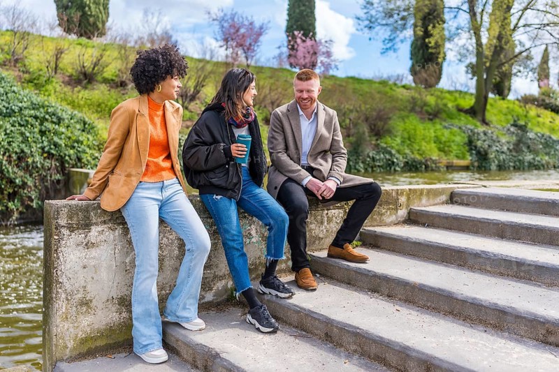 Three young professionals enjoying a break, chatting and laughing together by a canal in a city park