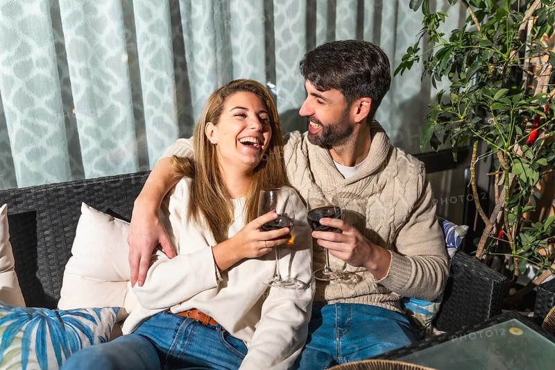 Cheerful couple enjoying a romantic evening, drinking wine and laughing together on a cozy terrace