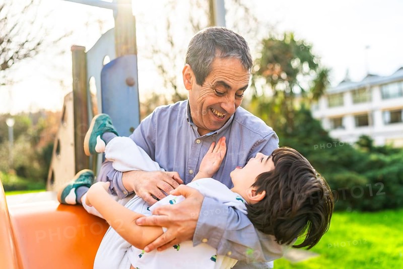 Grandfather holding his grandson and playing together at the playground, having a joyful and playful moment