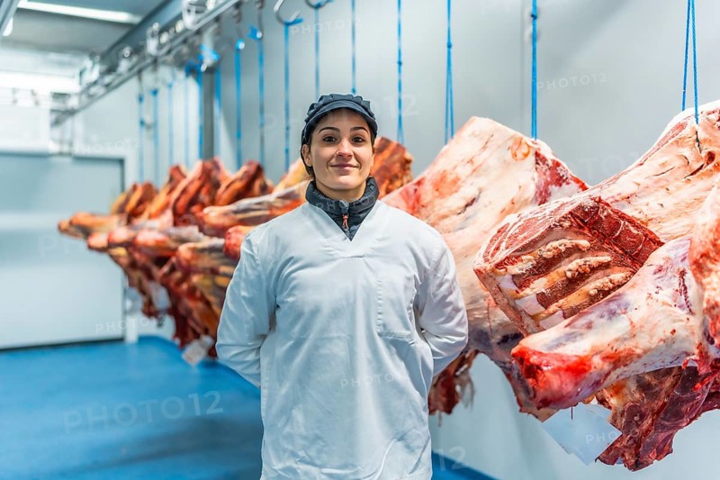 Three quarter length frontal portrait of a proud and happy woman butcher in a meat processing factory