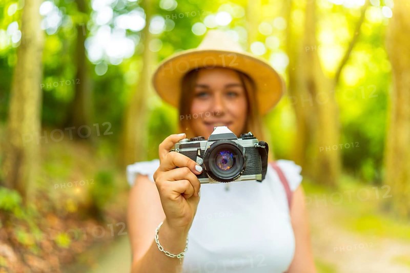 Portrait with selective focus on the camera in hands of a young female caucasian photographer in the forest