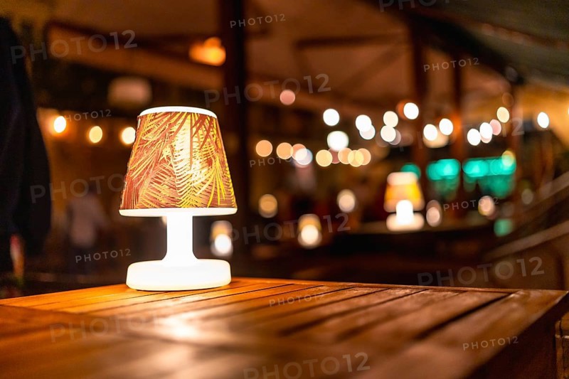 Soft, warm lighting creates a cozy atmosphere at a rustic wedding venue, highlighting elegant wooden tables and a charming lampshade design