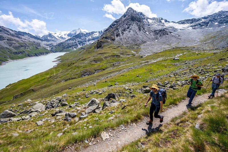 Three mountaineers on a hiking trail at a blue mountain lake, reservoir Lac des Dix, behind mountain peak Mont Blanc de Cheilon, Hérménence, Valais Alps, Valais, Switzerland, Europe