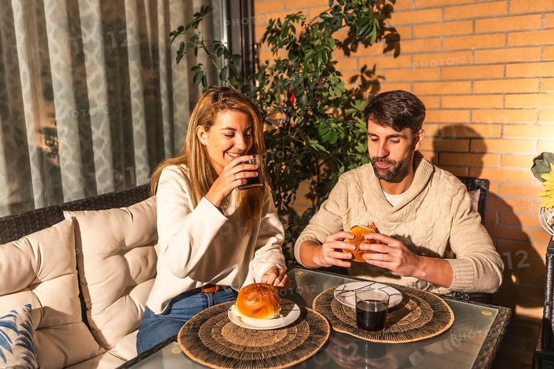 Smiling man and woman enjoying burgers and beverages on a cozy terrace, creating a warm and inviting atmosphere