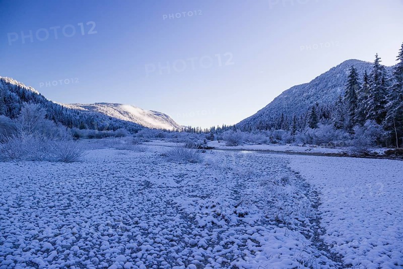 Isar valley in winter at temperatures of minus 18 degrees Celsius. Snow covered landscape with the Isar river flowing through. Some hoar frosted trees. Early morning