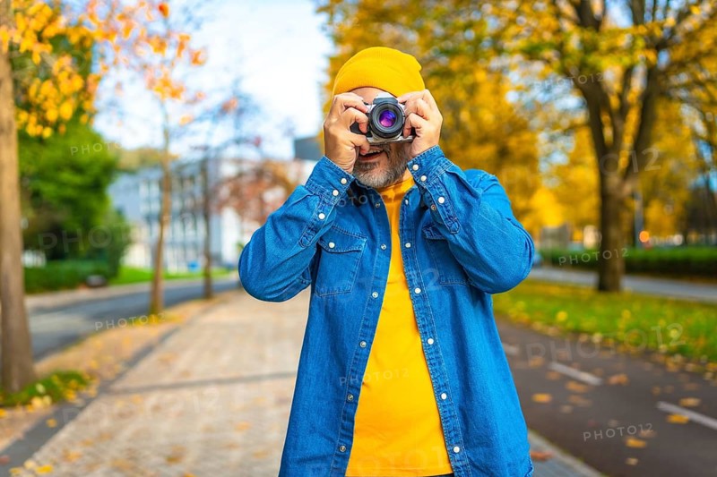 Frontal portrait of a mature modern man photographing in the city while visiting it in autumn